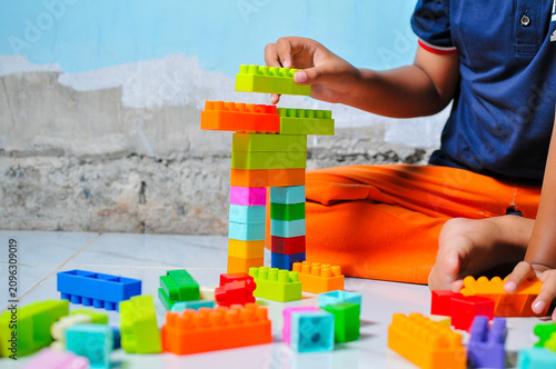Close up view of a kid playing and stacking colorful plastic toy building blocks on the floor, focusing on fine motor skills development and screen-free creative activity.