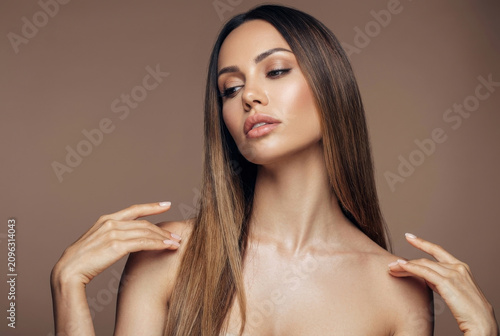 A sophisticated studio portrait capturing a moment of quiet elegance. A beautiful woman with sleek, long brown hair tilts her head slightly, her gaze cast downward in a serene expression