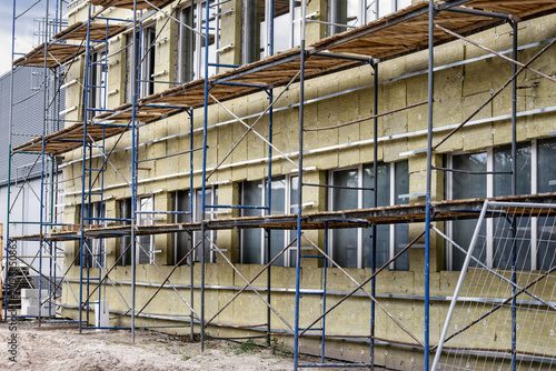 Fotografie Workers use scaffolding to insulate the facade of a building with mineral wool