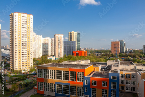 Modern residential district with colorful school building and high-rise apartment houses under blue sky