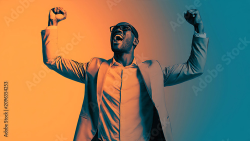 Excited successful businessman raising fists celebrating victory under vibrant colorful lighting