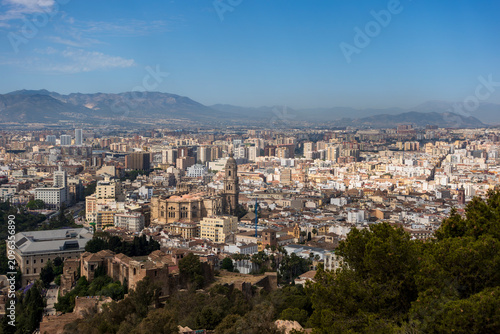 Expansive view of Málaga, Spain, featuring the Málaga Cathedral prominently in the center. The Alcazaba, a notable Moorish fortress, is visible with its distinct stone walls in the foreground
