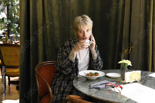 Stylish non binary person enjoying coffee in cozy cafe on a sunny afternoon