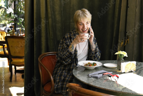 Young beautiful non binary person enjoys cozy time at cafe while chatting over coffee