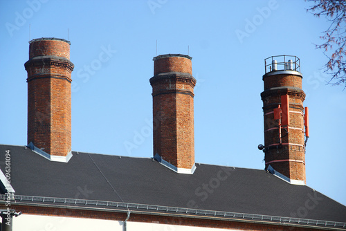 Three Historic Brick Industrial Chimneys Rising Above a Factory Roof