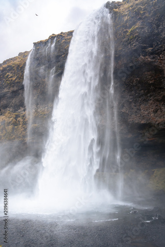 vertical photograph of Seljalandsfoss, a famous Icelandic waterfall south of Reykjavik, on a cloudy day