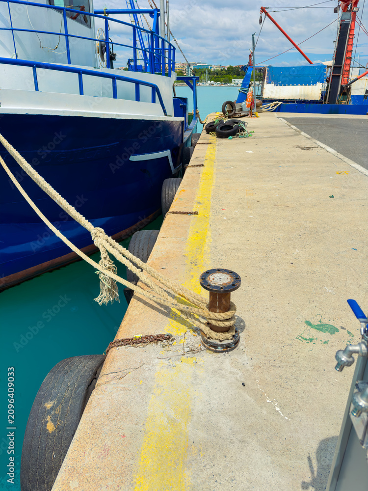 Fototapeta premium Boat is tied at the dock near the harbor with a rope attached to a pulley and a clear view of the turquoise water in the background