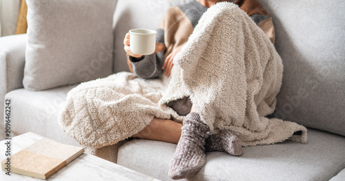 Obraz na plátně Woman sitting comfortably on a sofa, wrapped in a plush blanket and wearing warm