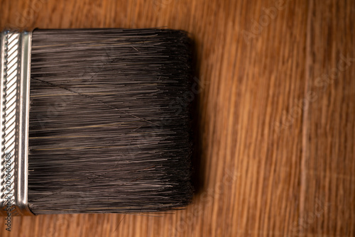 Paintbrush lying on varnished wooden floor texture. Detail shot emphasizing home renovation interior design services marketing campaigns commercial diy projects background