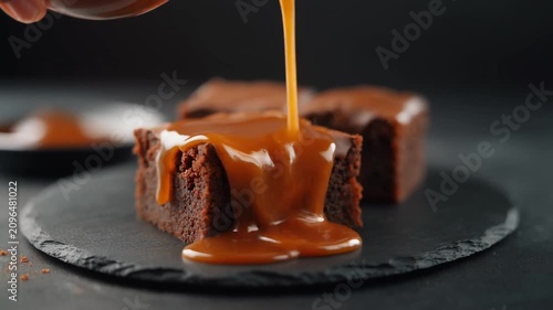 Chocolate sauce is poured over a rich, decadent brownie on a plate.
