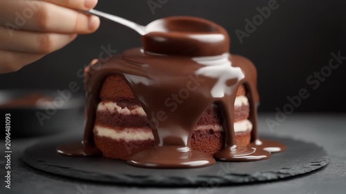 A hand drizzles rich chocolate sauce over a decadent layered chocolate cake on a plate.
