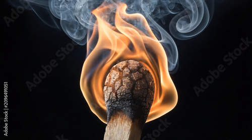 Burning match head with smoke on black background, close macro fire still life