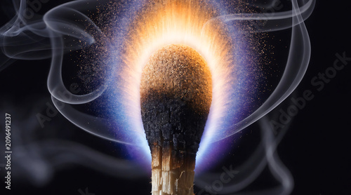Extreme macro photograph of wooden match burning with smoke and glowing flame on dark background