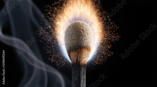 Burning matchstick with spark halo on black background