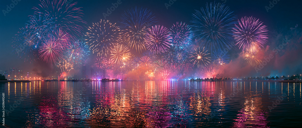 Obraz premium Celebration Fireworks over Riverside Cityscape: Vibrant Night Sky Reflections and Colorful Explosions