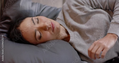 Woman reclining on bed settling and shifting hands in pullover hugging gray pillow for comfort