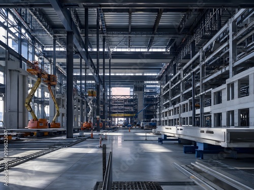 Industrial building construction site interior with steel frame structure. Heavy machinery and crane during facility development. Modern architecture engineering and infrastructure project.
