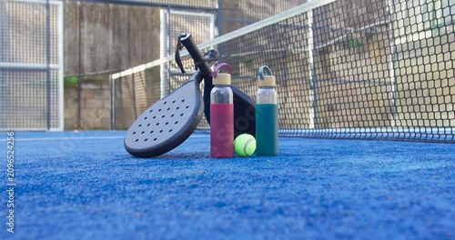 Padel racket and two reusable bottles are remaining on blue turf after match ends, ball resting