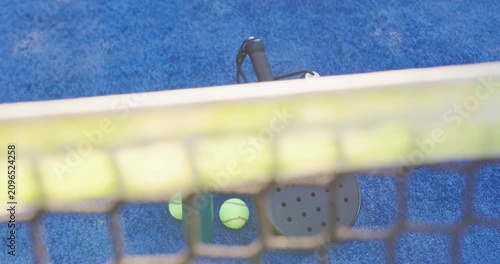 Camera lowering is revealing padel racket, three balls and bottles on blue court to showcase gear