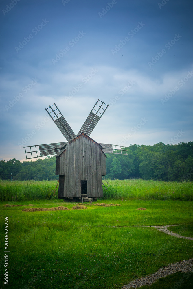 Obraz premium Rustic wooden windmill stands in a lush green field under a cloudy sky.