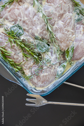 Chicken marinating in Greek yogurt with fresh rosemary and herbs in a glass container. Healthy barbecue preparation combines tender poultry with natural ingredients for summer outdoor cooking.