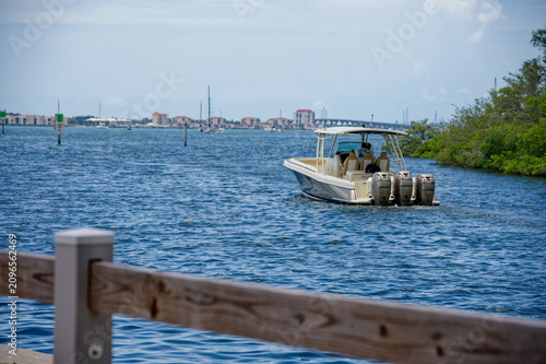 Canvas Print A motorboat with triple outboard engines cruises along calm blue water past a wo