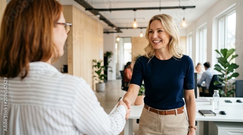 Two smiling businesswomen shaking hands, showing collaboration and agreement in a modern office environment