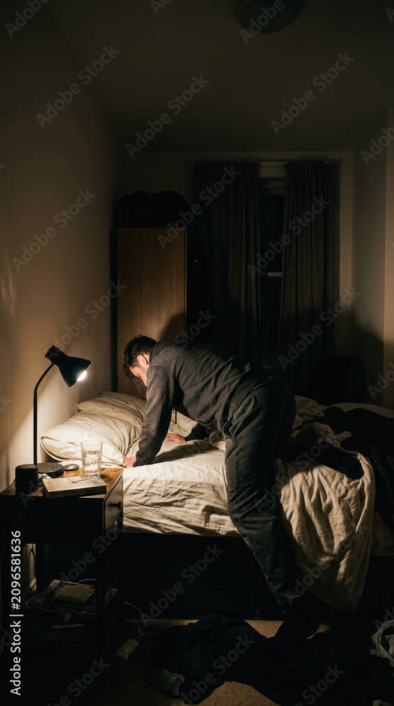 Fototapeta premium Man Searching Through Messy Bedroom In Dim Light Of A Desk Lamp