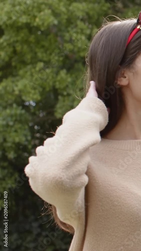 Vertical video: Lifting arm, woman fixing red headband tucking at hedge in tan jumper, copy space