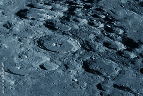Moon dominates dark sky, detailed craters visible. Surface shows gray and blue tones. Elements of this image furnished by NASA