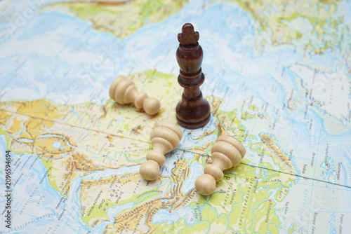 Fotografie Black king chess piece standing on a map while white bishops lie fallen, symboli