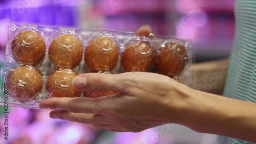 Close up of female hands holding and inspecting plastic container of fresh brown chicken eggs in a supermarket. Customer choosing produce in grocery store department. Healthy eating concept.