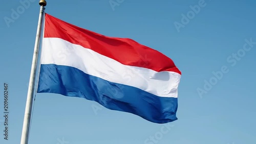Flag of the netherlands waving in the wind against a clear blue sky