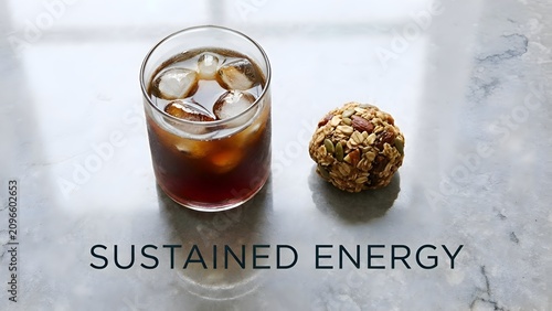 Cold iced coffee in a glass next to a nutritious oat and nut energy ball on a white marble tabletop providing a balanced snack for sustained energy throughout the day