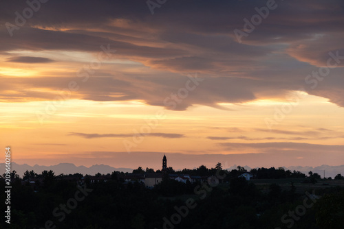 Dramatic Summer Sunset Over Rural Village in Piedmont, Italy, with Church Tower Silhouette