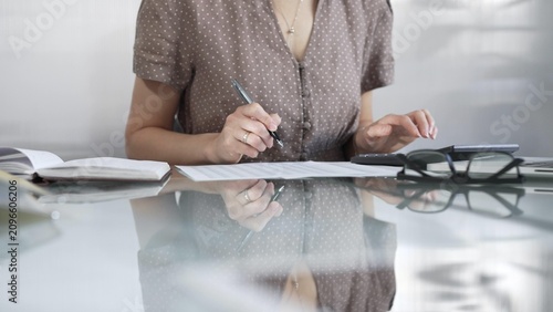 Принти на полотні Businesswoman accountant, wearing brawn dotted blouse, is using a calculator to crunch numbers and jotting down meticulous notes, at sleek glass desk in a contemporary office