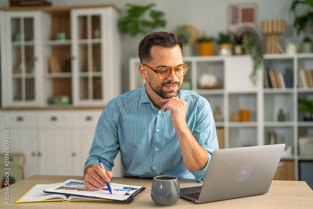 Obraz premium Man working remotely at home office desk checking data
