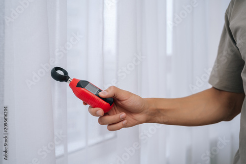 Close-up hand of unrecognizable man measuring natural light by window with digital luxmeter, testing illumination levels for optimal home brightness, energy efficiency and comfortable daylighting.