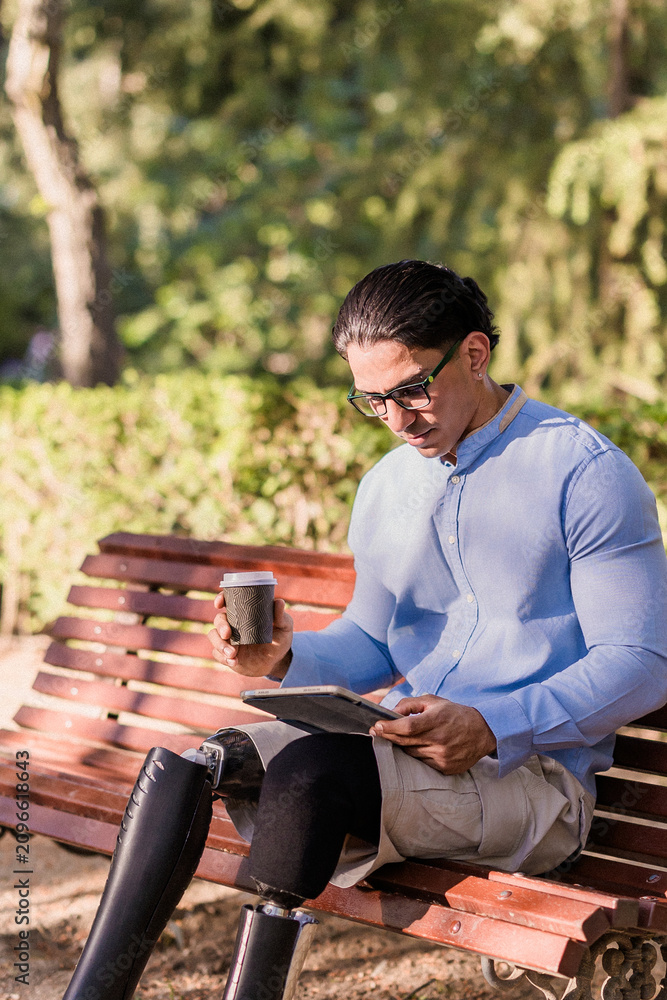 Fototapeta premium Latino man with prosthetic legs enjoying coffee break in park