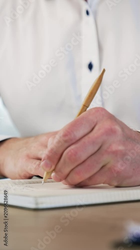 Hands of a male wearing white shirt taking notes into the paper book. Close up view of a handwriting with a ball pen. Vertical video