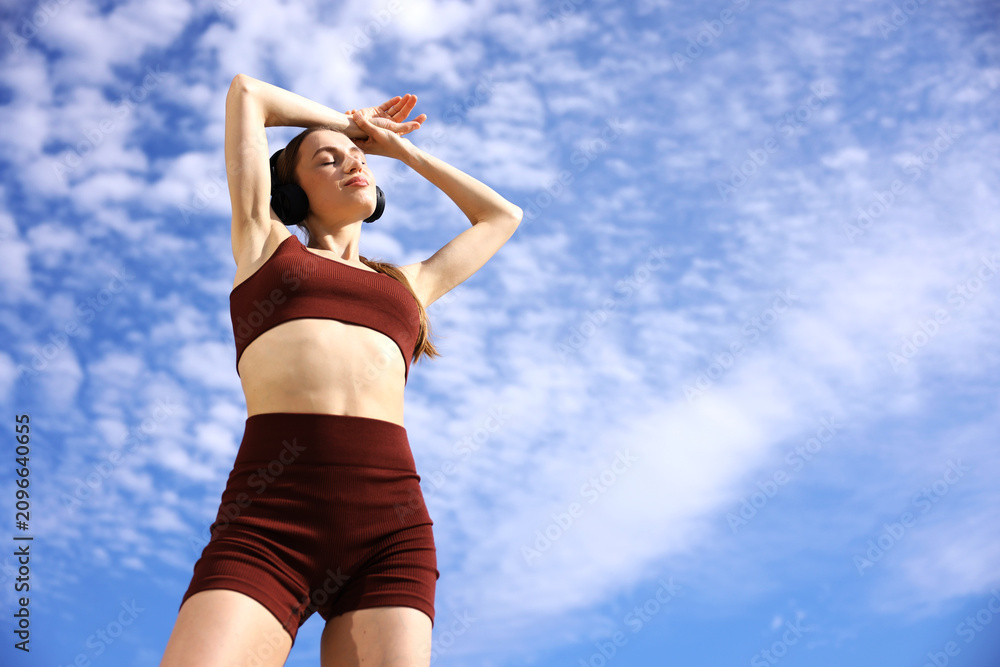 Obraz premium Woman in sportswear with headphones outdoors under blue sky, low angle view. Space for text