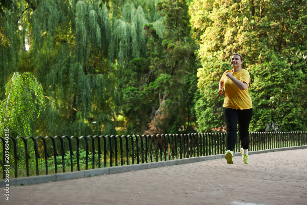 Obraz premium Smiling overweight woman running in park. Space for text