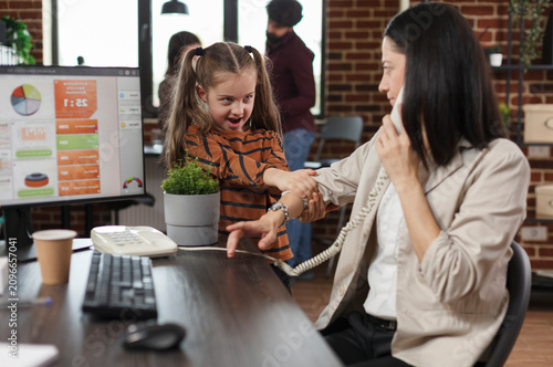 Foto Working mother gives financial advice by phone while a playful daughter interrupts her finance office call and customer consultation