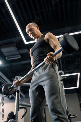 Muscular man lifting barbell during strength training in gym