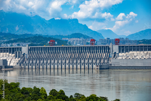 A view of the large concrete dam structure located within the Three Gorges Reservoir Area in China showing the calm water and mountain landscape under a blue sky