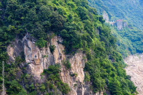 A view of the steep green mountains and rocky cliffs situated in the Three Gorges Reservoir Area in China showing a small building on the hillside