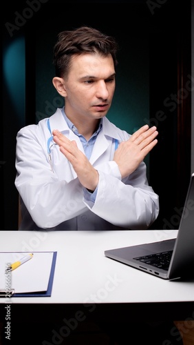 фотографія Doctor in a white lab coat and stethoscope making a stop gesture with crossed ha