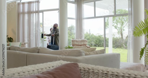 African American couple entering through sliding door, pulling wheeled suitcase, arriving home