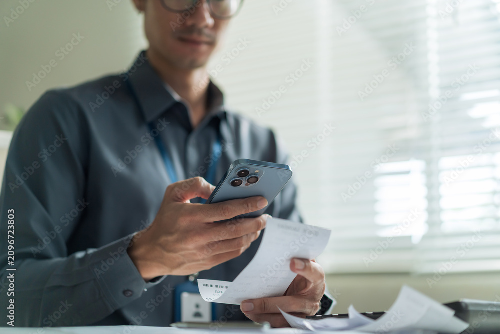 Fototapeta premium Close-up of office worker using smartphone to scan receipt and financial bill for mobile payment at desk.