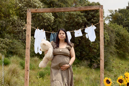 Medium Shot of Pregnant Hispanic Woman with Teddy Bear and Baby Clothesline